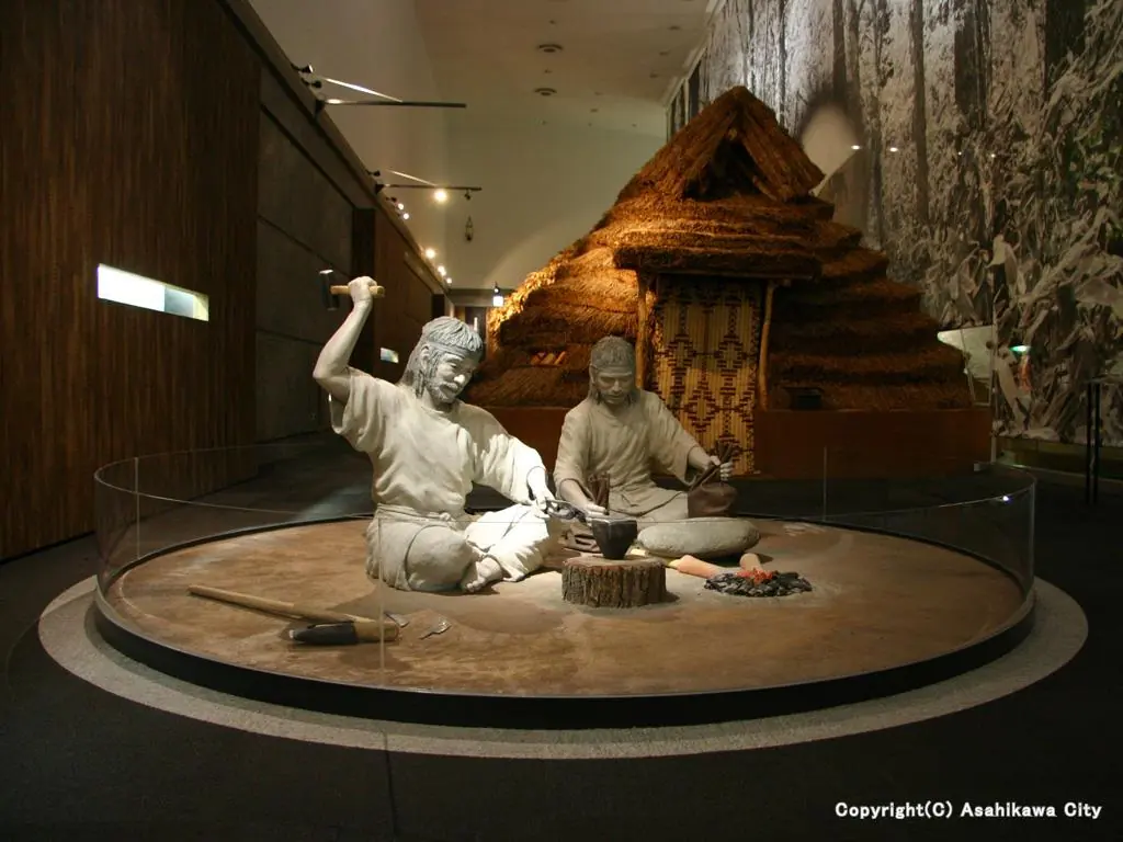 茅葺きの家の前で作業する二人の人形(旭川市博物館の展示)