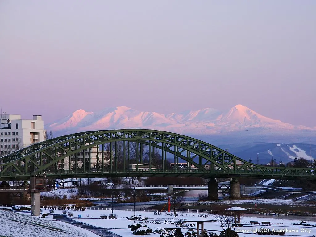 ピンク色の空と雪山を背にした旭橋の緑の鋼のアーチ